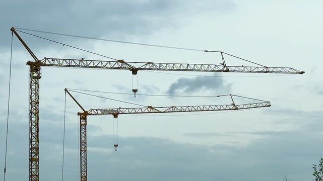 Twin tower cranes stretching across a cloudy sky above an urban construction site