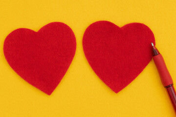 Obraz premium Two red hearts on bright yellow felt with pen for romance