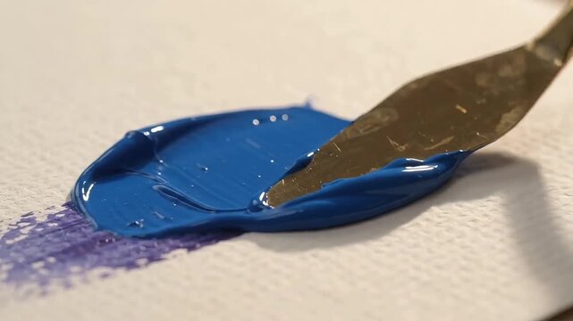 Palette knife spreading vibrant blue gel paint on textured paper