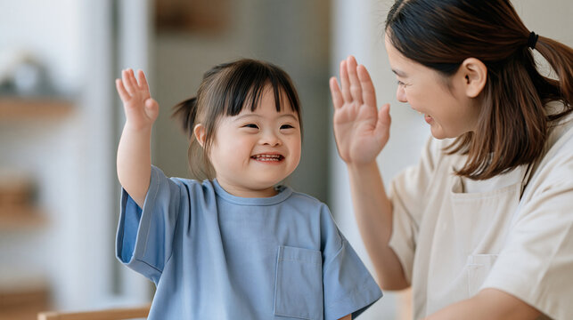 Thai child with Down syndrome celebrating high five with pediatric occupational therapist following successful fine motor skills session, early intervention therapy, developmental