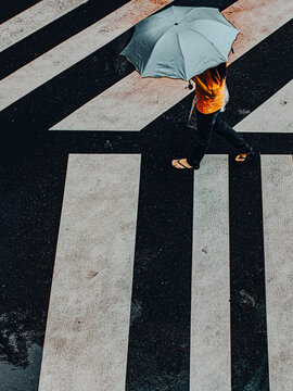 Aerial View of Person in Orange Shirt Holding Grey Umbrella Crossing Wet Street