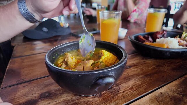 person stirring traditional colombian soup (mondongo) bowl with spoon on wooden table