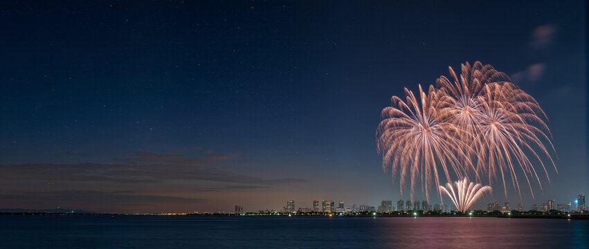 Colorful fireworks exploding over a dark city skyline and river at night. Celebration background