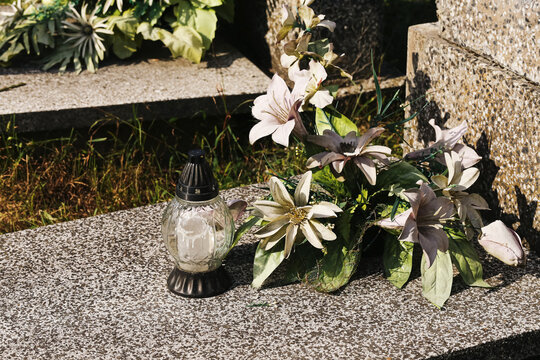 Memorial candle beside artificial flowers background. Grave decoration rests on stone surface. Cemetery remembrance mourning tribute loss funeral and commemoration symbolism.