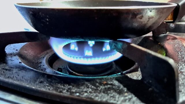 Blue flame heats a frying pan as a gas stove burner ignites.