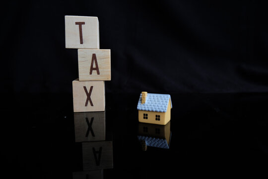 Concept of property tax based on the value of a house, building, or land, as well as local development tax: the word "tax", a house model on a dark background.