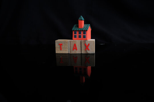 Concept of property tax based on the value of a house, building, or land, as well as local development tax: the word "tax", a house model on a dark background.