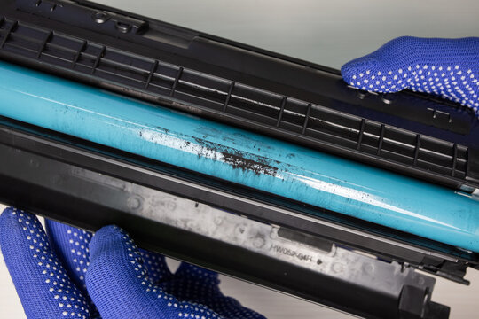 A technician is holding a laser printer cartridge with an exposed drum on which poor-quality toner has baked on.