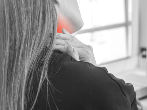 Close up view of woman massaging aching neck with red highlight pain zone. Tired corporate worker suffering from cervical osteochondrosis or cold muscle spasm at desk. Sedentary office job trauma.