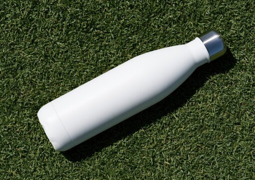 Sleek white reusable water bottle with metal cap, resting on lush green grass