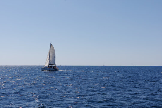 Sailboat moves across open blue sea beneath a clear sky with generous copy space. Concept of sailing, maritime recreation, navigation, freedom, adventure and summer sea travel.