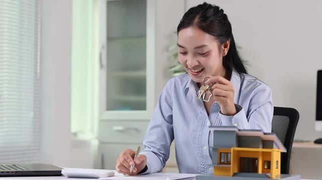 Real estate agent signing a contract and holding house keys with a miniature home model on her office desk, representing a successful property sale, mortgage, or lease agreement