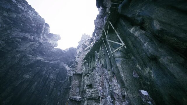 Vertical rock shaft with metal ladder framing rugged limestone walls, mosscovered ledges, damp textures and narrow sky opening above moody overcast light