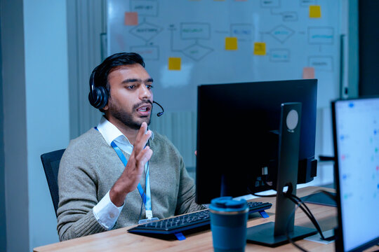 Dedicated Indian call center agent using headset to assist customer late at night in modern office