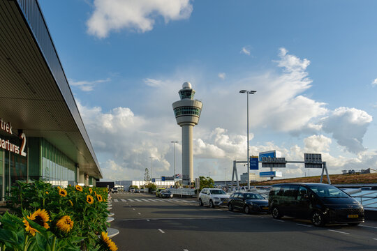 August 21, 2026, Amsterdam, Netherlands - Exterior view of Amsterdam Schiphol Airport terminal with air traffic control tower and sunflowers