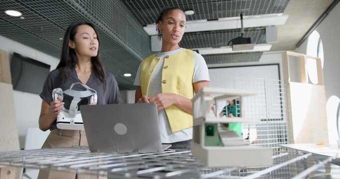 Two Women Architects Collaborating in Modern Office Space, using VR headset and Laptop