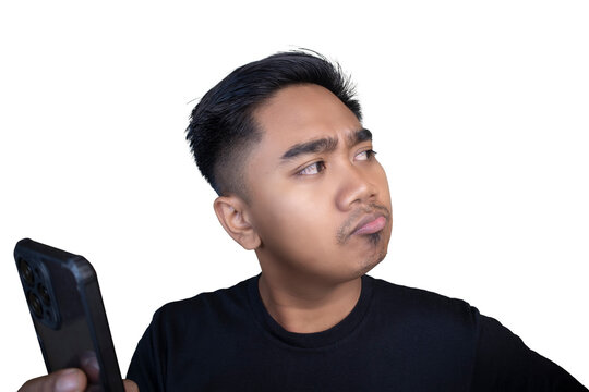 Skeptical Indonesian man wearing a black t-shirt looking away sideways while holding a mobile phone with a pouting expression against a white background.