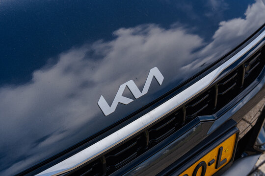 August 21, 2026, Amsterdam, Netherlands - Close-up of the new Kia logo on the hood of a dark blue car with cloud reflections
