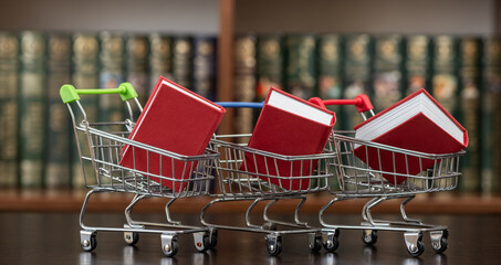 Red books in a miniature shopping cart against a background of bookshelves. © Max Zolotukhin