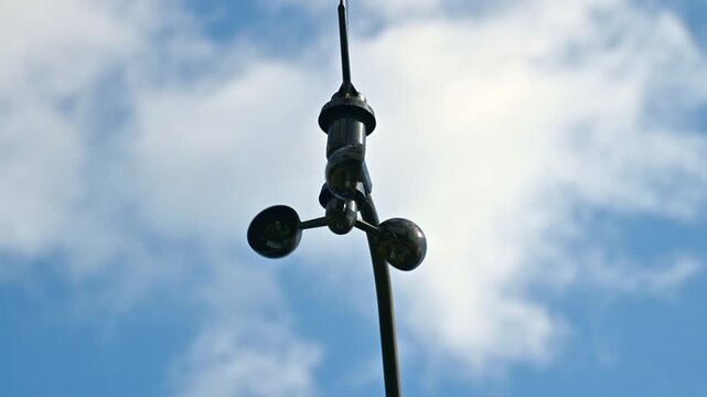 Cup anemometer rotating on mast against cloudy blue sky