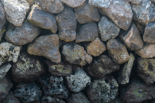 Textured volcanic stone wall with interlocking grey and brown rustic basalt rocks.