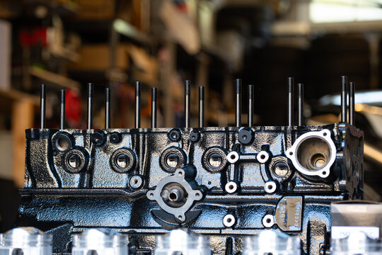 Black painted engine block with installed head studs resting on a workbench inside an automotive repair shop.