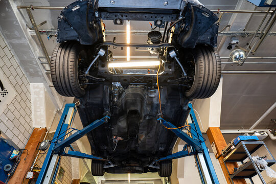 Wide angle undercarriage view of a car raised high on a hydraulic lift inside an auto repair shop.