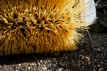 Cylindrical sweeper brush with dense bristles resting on loose gravel and debris, representing mechanical road cleaning attachments and paved area maintenance © K