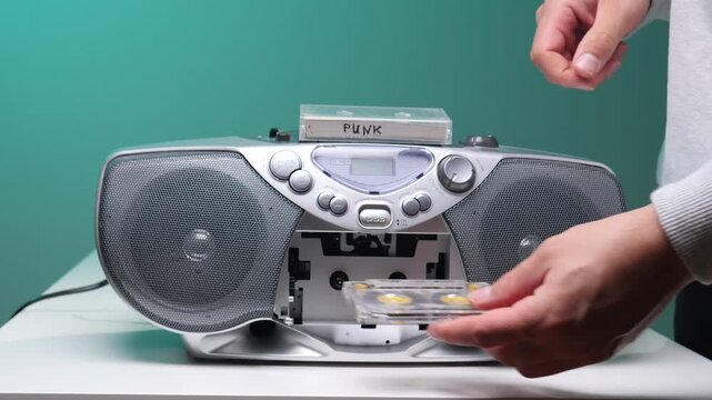 Hand pressing a button on a classic silver boombox, playing a cassette tape labeled punk, embodying 90s audio nostalgia and retro music culture against a teal background