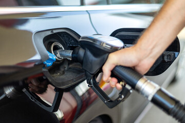 Refueling a Silver Car at a Gas Station. Close-up of a hand holding a fuel pump nozzle inserted into the open fuel port of a silver car at a gas station. © Iryna