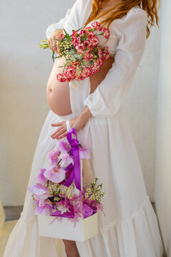 Pregnant woman in flowing white dress with colorful flowers in artistic maternity portrait. Artistic maternity portrait showing a pregnant woman in a flowing white dress with colorful flowers arranged