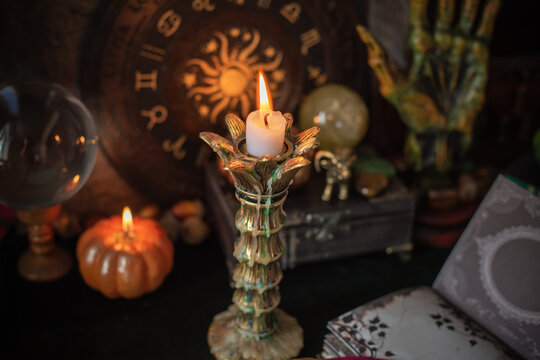 Burning candle in vintage candlestick on mystical altar with crystal ball, zodiac wheel, old spell books and dip pen 