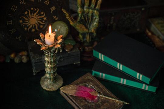 Burning candle in vintage candlestick on mystical altar with crystal ball, zodiac wheel, old spell books and dip pen 