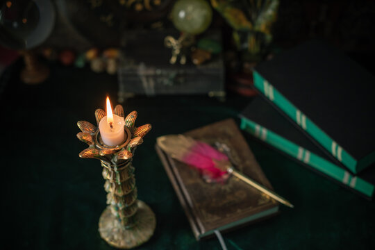 Burning candle in vintage candlestick on mystical altar with crystal ball, zodiac wheel, old spell books and dip pen 