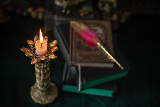 Burning candle in vintage candlestick on mystical altar with crystal ball, zodiac wheel, old spell books and dip pen 