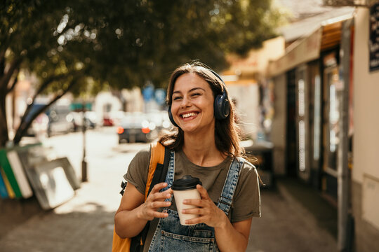Young woman enjoying music and coffee on city street