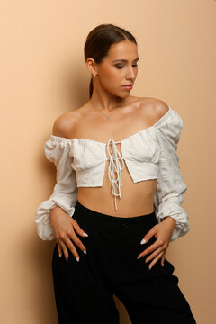 Studio shot of a woman looking up and away, wearing a white puff sleeve crop top, on beige background