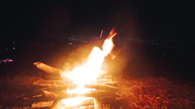 Bright bonfire burning outdoors at night with distant city lights