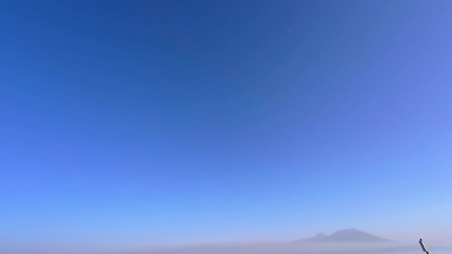 Clear blue sky with distant mountain silhouette and subtle moon above horizon