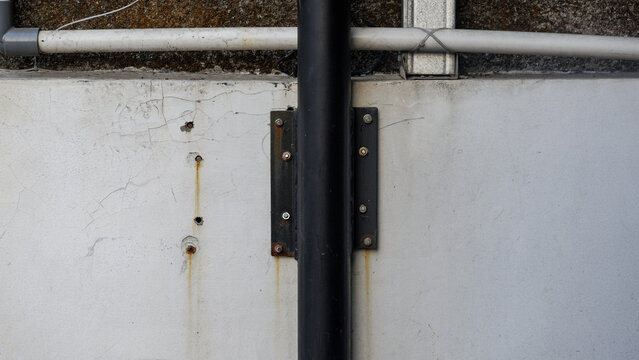 Industrial building wall detail featuring a black drainage pipe bracketed onto weathered grey concrete with rust marks.