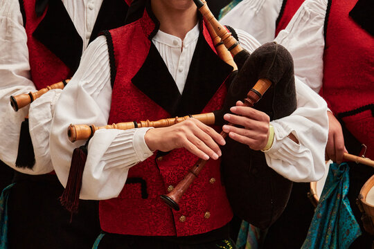 Close-up of a musician playing a traditional Galician bagpipe, or gaita, while wearing a red, white and black folk costume during a cultural music performance.