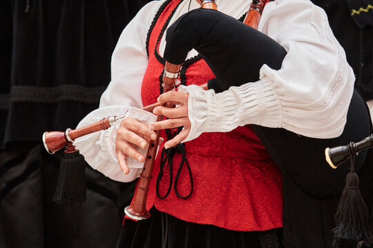 Close-up of a musician&rsquo;s hands playing the chanter of a traditional Galician bagpipe, or gaita, while wearing a red and white regional folk costume.