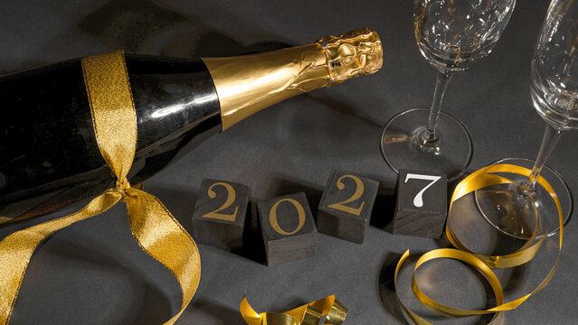 New Year 2027 New Year's Eve celebration holiday greeting card background - Black cubes with year, sparkling wine or champagne bottle and glasses on black table, top view