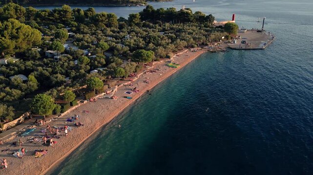 Orbiting counterclockwise aerial shot of Kovacine camp beach with the Cres harbour entrance in the background, town Cres, island Cres, Croatia