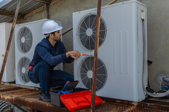 Air conditioner repairman, technician checking air conditioner, measuring device for refilling air conditioner. HVAC service technician using gauges to check refrigerant and add refrigerant.