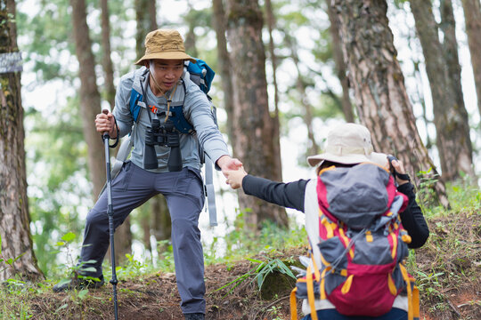 Male hiker reaches down to help his partner up a steep forest slope