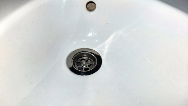 Ceramic bathroom washbasin drain metal hole. Close up view of white sink basin plumbing fixture