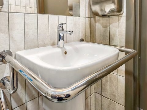 Modern ceramic bathroom sink with metal grab bar for accessibility. Accessible washbasin design for public restroom