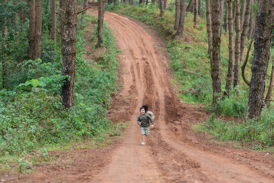 A young girl runs down a winding forest road in the distance