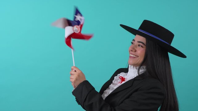 Young smiling woman in traditional huasa dress holding a Chilean flag pinwheel on turquoise background
